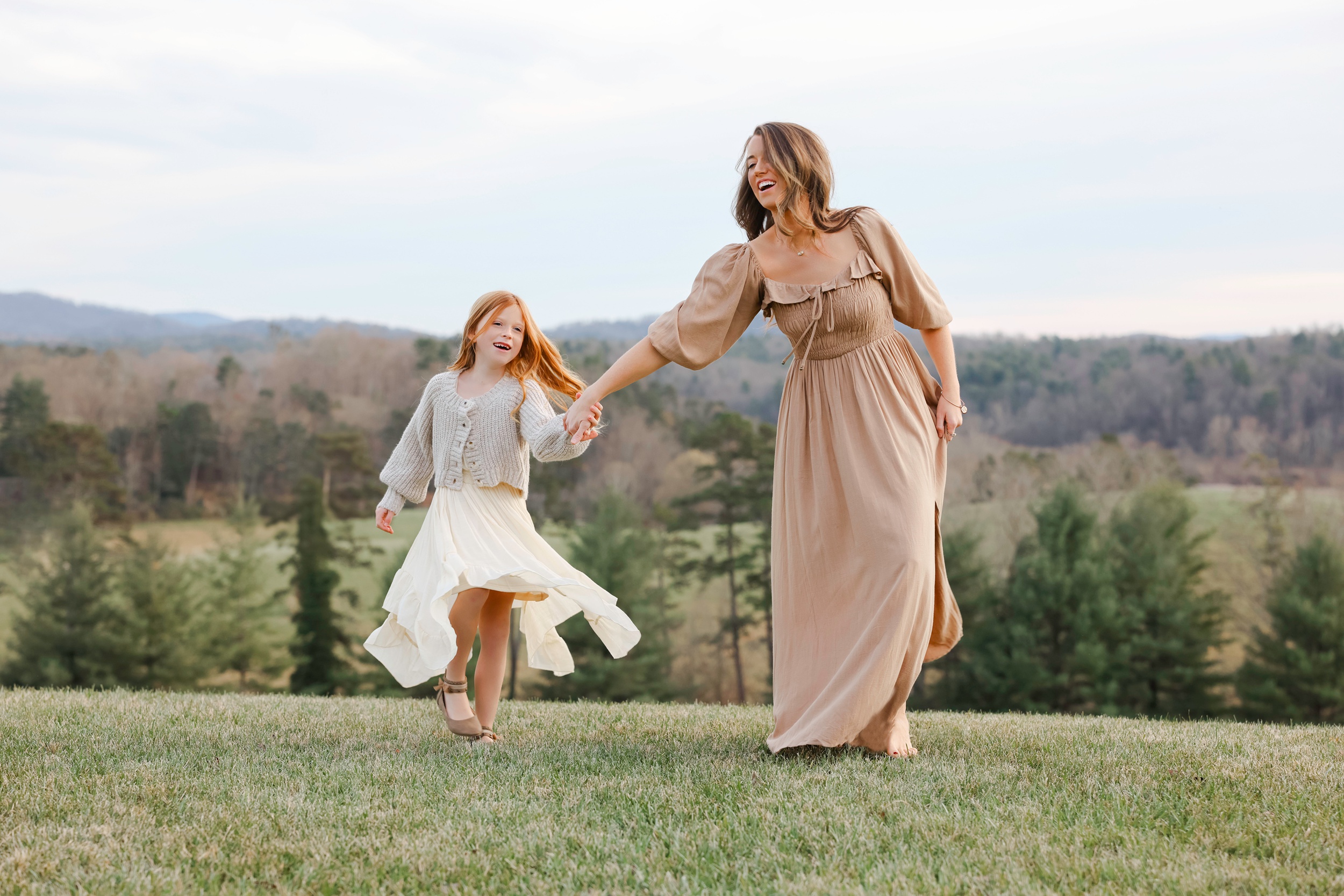 A Mom In A Brown Dress Plays And Runs With Her Laughing Young Daughter On A Mountain Meadow After Meeting Asheville Doulas