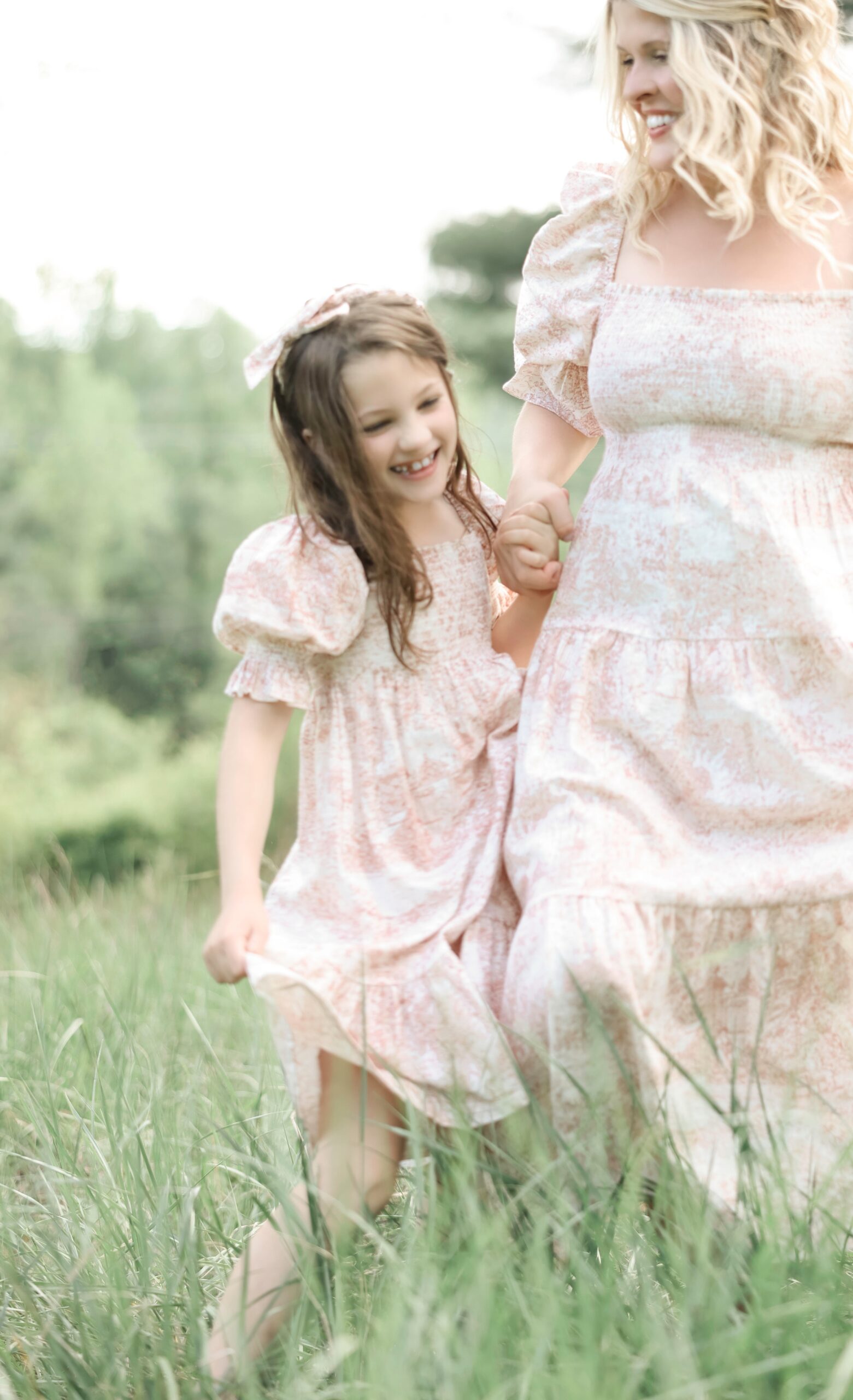 A Happy Young Girl Plays In A Field Of Tall Grass With Mom In Matching Pink Dresses Thanks To Asheville Fertility Clinics