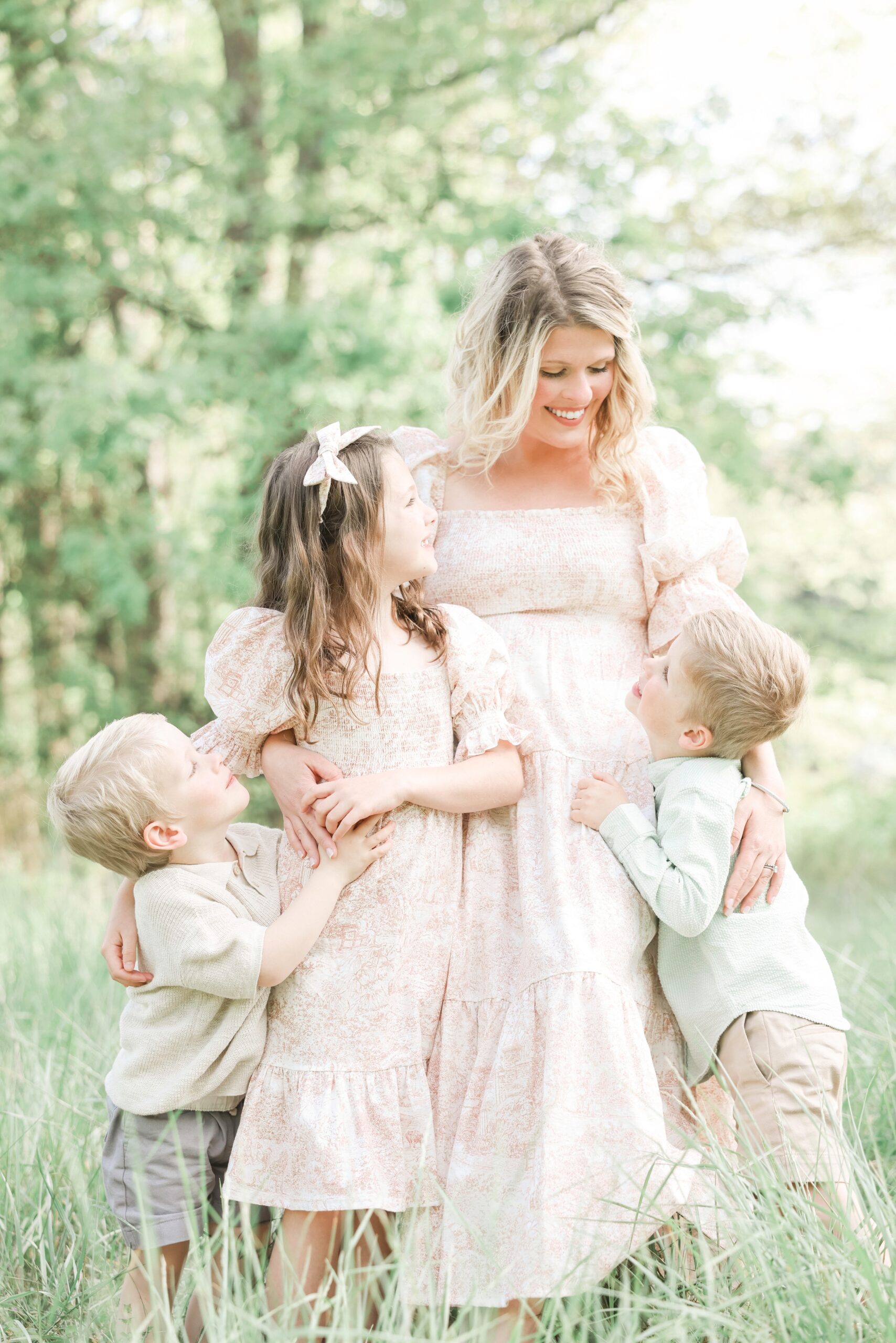 A Happy Mom Is Hugged By Her Three Toddlers In A Pink Dress Matching The Oldest Daughter In A Pasture Thanks To Asheville Fertility Clinics